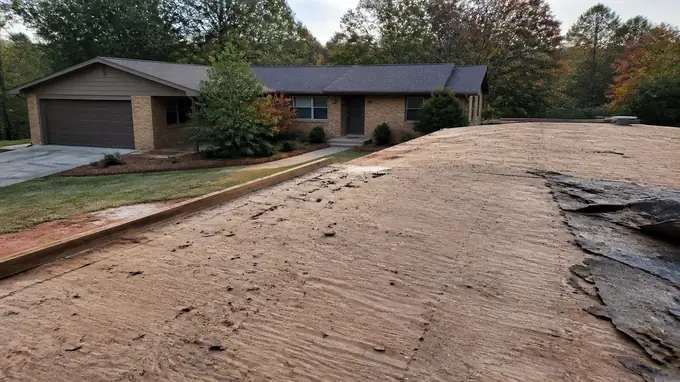 The stripped roof deck sits exposed after old shingles and felt are removed. at a buff-brick ranch home in Madison, WI, in early morning light.